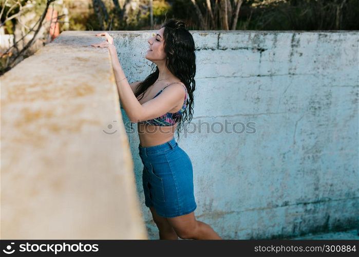Smiling young brunette woman with bikini in an old empty pool watching over the edge
