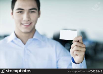 Smiling young businessman holding a business card and looking at camera