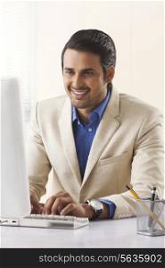 Smiling young businessman using desktop PC at office
