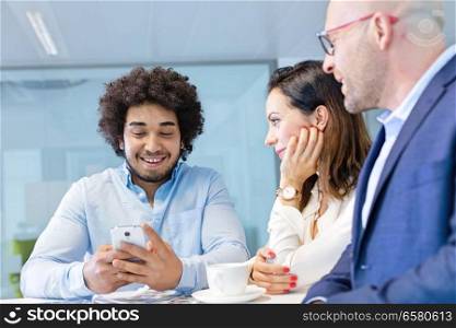 Smiling young businessman using mobile phone with colleagues in office