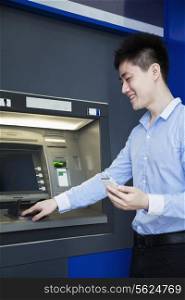 Smiling young businessman withdrawing money from the ATM