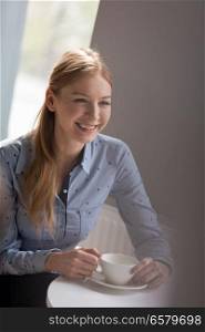 Smiling young businesswoman having coffee at table in office