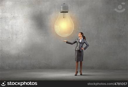 Smiling young businesswoman holding light bulb in palm. Present your idea