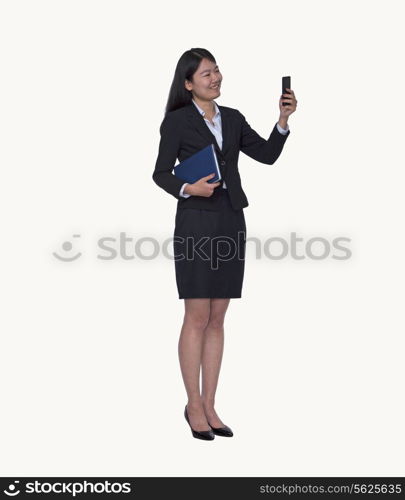 Smiling young businesswoman looking at her phone, full length, studio shot