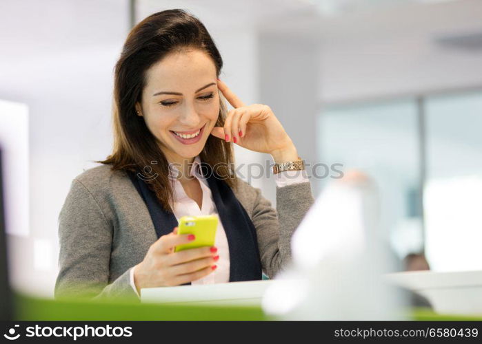 Smiling young businesswoman reading text message on smartphone at office