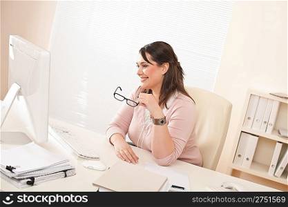 Smiling young businesswoman sitting at office watching computer screen