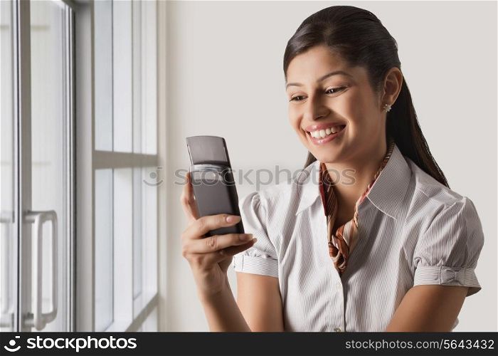Smiling young businesswoman text messaging at office