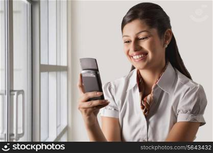 Smiling young businesswoman text messaging at office