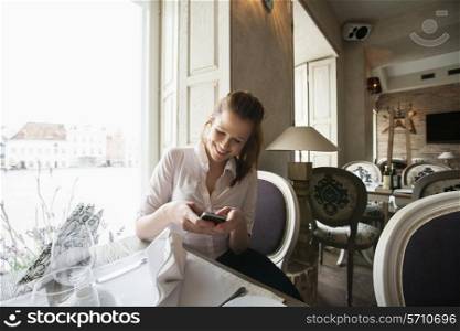 Smiling young businesswoman text messaging on cell phone at restaurant table