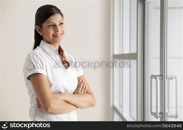 Smiling young businesswoman thinking with arms crossed at office