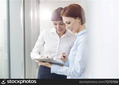 Smiling young businesswoman using digital tablet by colleague at office