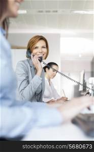 Smiling young businesswoman using landline phone in office