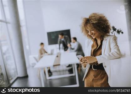 Smiling young businesswoman using mobile phone in modern office