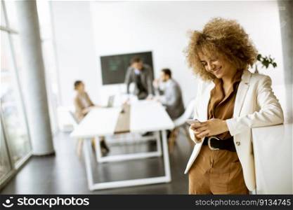 Smiling young businesswoman using mobile phone in modern office