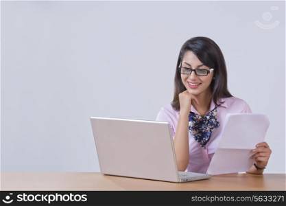 Smiling young businesswoman working on laptop at desk in office