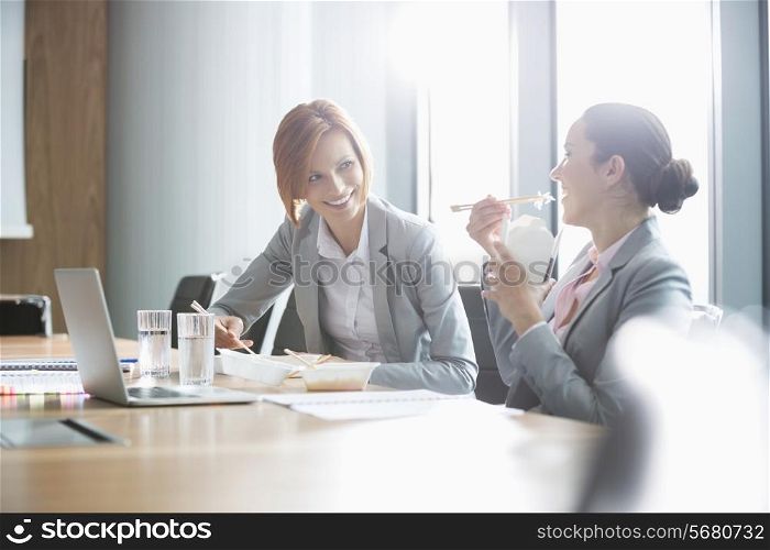 Smiling young businesswomen having lunch at table in office