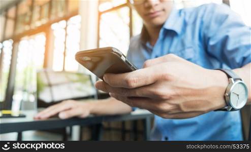 Smiling young casual business man with mobile phone in the hand in office.