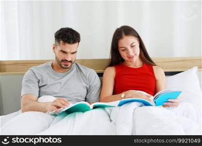 Smiling Young Caucasian couple love is reading books together on the bed in bedroom. Married family and lifestyle at home on holiday concept