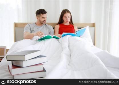 Smiling Young Caucasian couple love is reading books together on the bed in bedroom. Married family and lifestyle at home on holiday concept