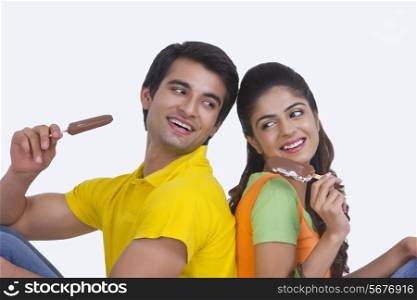 Smiling young couple enjoying chocolate ice-cream bars over white background