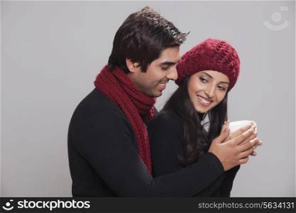 Smiling young couple holding cup over grey background