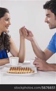 Smiling young couple holding hands while having coffee against white background