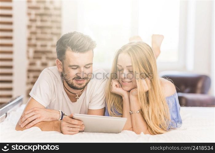smiling young couple lying bed looking digital tablet bedroom