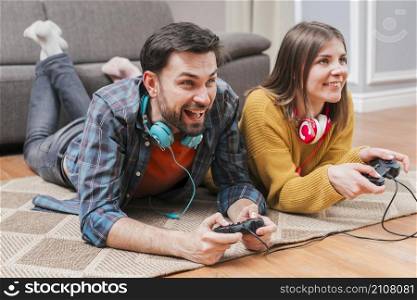 smiling young couple lying floor playing video game with joystick home