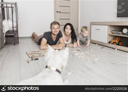 smiling young couple lying hardwood floor with their son looking white dog