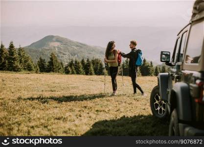 Smiling young couple preparing hiking adventure with backpacks by terrain vehicle