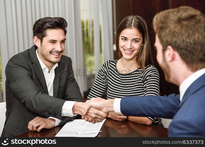 Smiling young couple shaking hands with an insurance agent or investment adviser