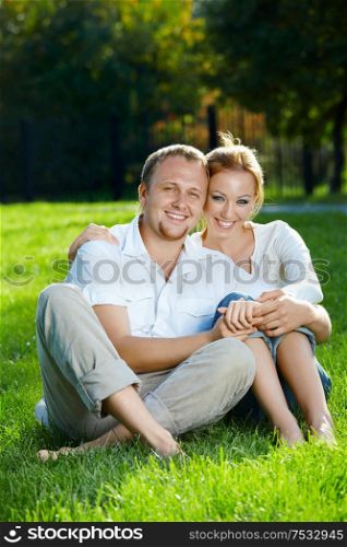 Smiling young couple sits on a lawn in a summer garden