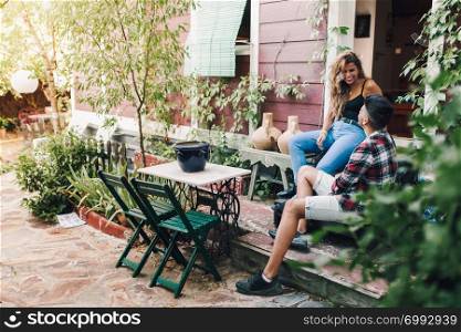 Smiling young couple sitting in the garden chairs near their wooden house with their smart phone