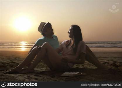 Smiling young couple sitting together on beach at sunset