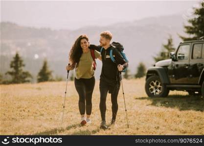 Smiling young couple starting walking with backpacks over green hills