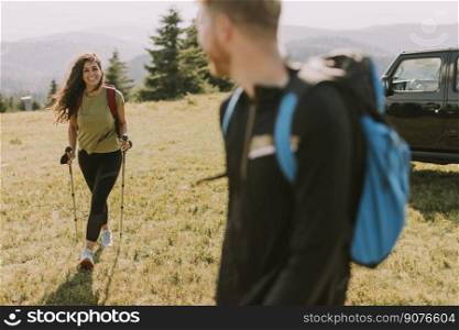 Smiling young couple starting walking with backpacks over green hills