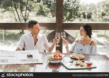smiling young couple toasting wine glasses with apple fruits table