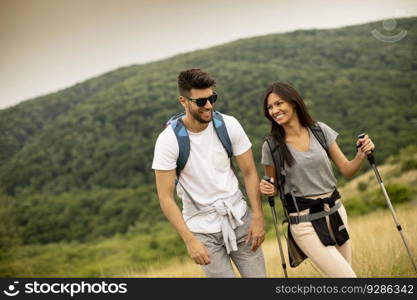 Smiling young couple walking with backpacks on a green hills at a summer day