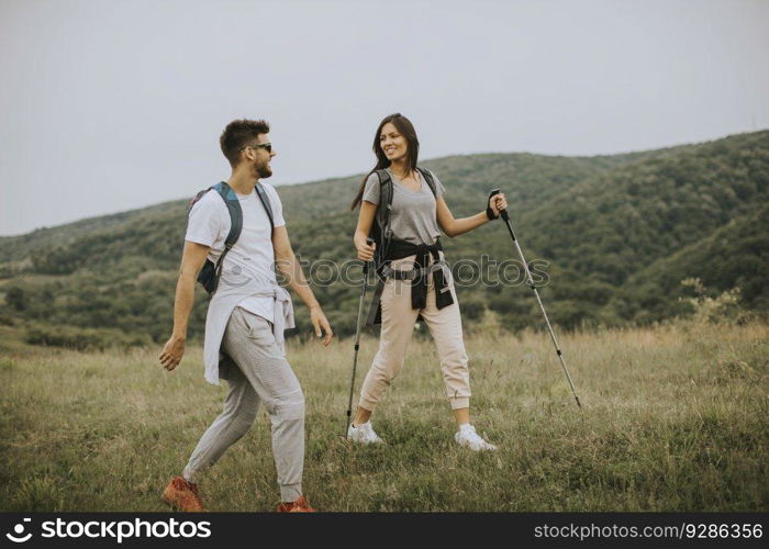 Smiling young couple walking with backpacks on a green hills at a summer day