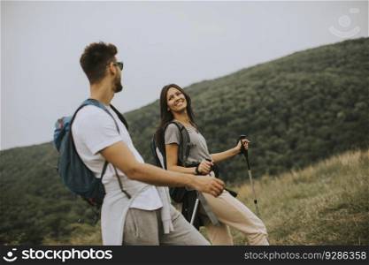 Smiling young couple walking with backpacks on a green hills at a summer day