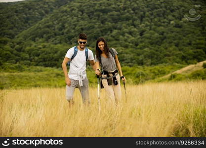 Smiling young couple walking with backpacks over green hills