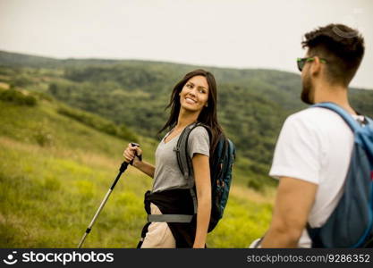 Smiling young couple walking with backpacks over green hills