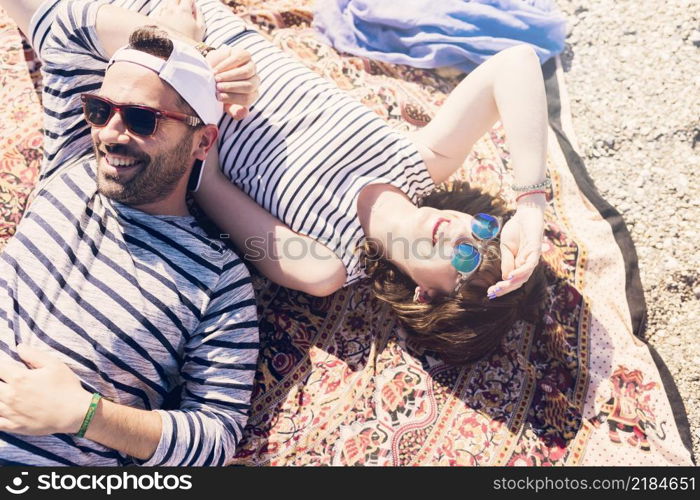 smiling young couple wearing sunglasses lying blanket