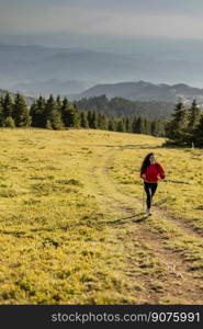 Smiling young curly hair woman walking with backpack over green hills