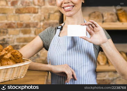 smiling young female baker showing white visiting card bakery shop
