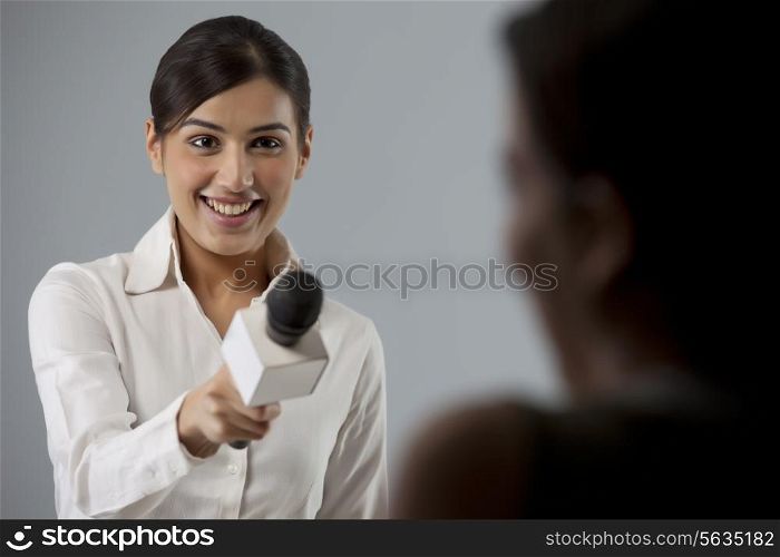 Smiling young female reporter taking interview of a person