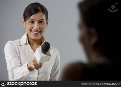 Smiling young female reporter taking interview of a person