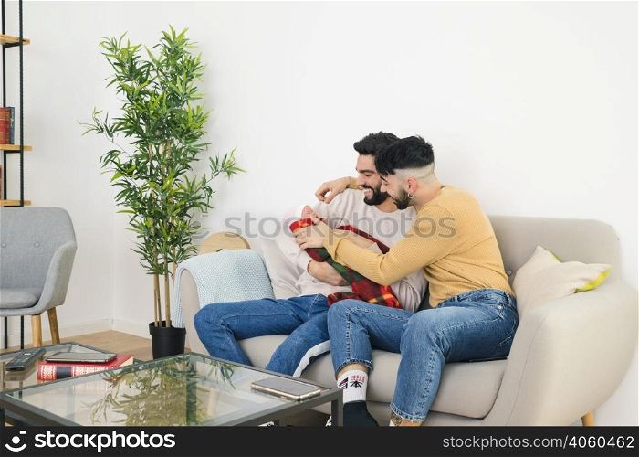 smiling young gay couple sitting sofa loving their baby