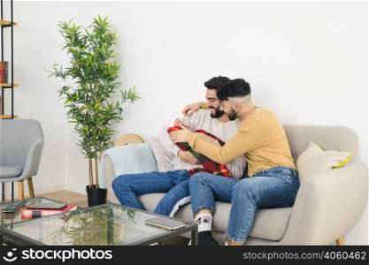 smiling young gay couple sitting sofa loving their baby