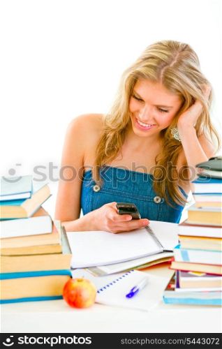 Smiling young girl reading sms on mobile instead of doing homework&#xA;